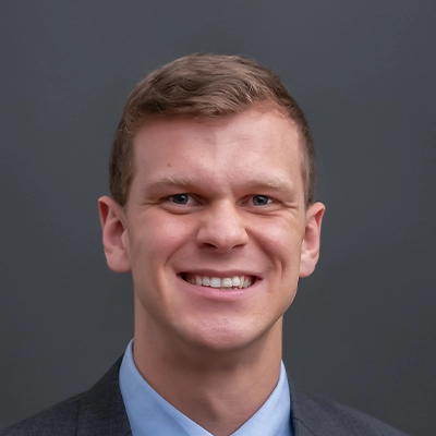 Chiropractor Adam Considine Smiling In Front Of Grey Background
